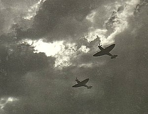 Two Spitfire single-seat piston-engined fighters in flight, silhouetted against cloud