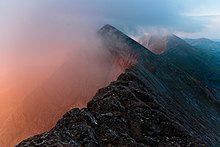 a series of jagged mountain peaks with a pinkish fog rising on the left side