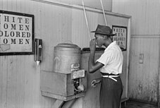 A drinking fountain from the mid-20th century labelled "Colored" with an African-American man drinking