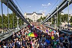 Large group or parade of people walking across bridge away from palace-like building