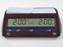 A brown chess clock with blue buttons along the bottom. A digital display shows the time remaining for each side