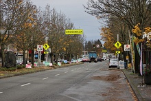 The view looking down a one-way street with two lanes and a pullout curb for parking. A crosswalk with signs and signals is seen at the center of the image, along with a line of political campaign signs.