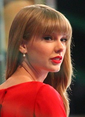 Taylor Swift performing live on a banjo, wearing a beige blouse and pigtails