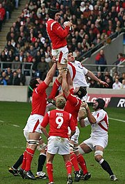 A Welsh player grasping the ball while being held in the air by his teammates following a line-out