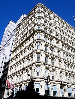 The southeast facade, as seen from ground level at Nassau and Fulton Streets. The upper floors are shown, and contain a rounded corner and cast-iron details.