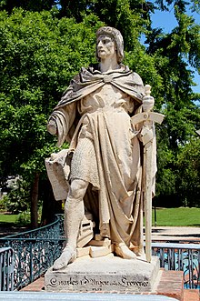 A middle aged man who wears a hauberk covered by coat and holds a sword