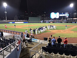 Men in white baseball uniforms celebrating on a green baseball field at night