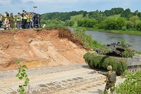 A tank driving out of water, people around watching