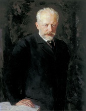 A middle-aged man with grey hair and a beard, wearing a dark suit and staring intently at the viewer