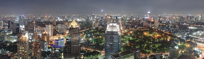 An expansive cityscape with several skyscrapers in the foreground, a park in the centre, and a large group of buildings across the park