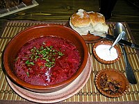 Borscht sprinkled with parsley, served with a dollop of sour cream and a slice of rye bread