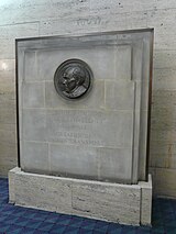 A stone memorial inset with a circular bronze relief side profile portrait and incised words "THE RT HON. LORD ASHFIELD P.C. 1874-1948 CREATOR OF LONDON TRANSPORT"