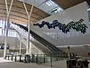 Airport Central station interior viewed from station concourse. The interior consists of white walls with large windows high up.