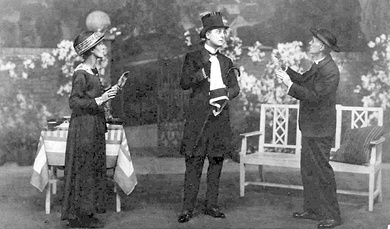 stage scene with man in full mourning costume centre, woman to his right and man in clerical garb to his left