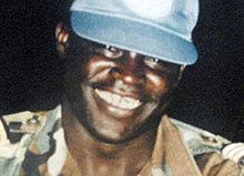 A smiling soldier with a blue cap and captain rank insignia