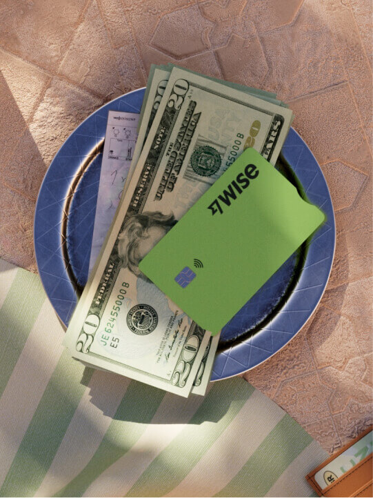 A plate sits on a table, with USD cash and a Wise card.