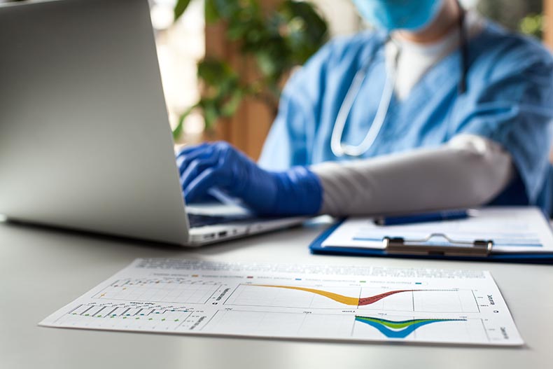 Photo of healthcare worker at desk with laptop and printed reports