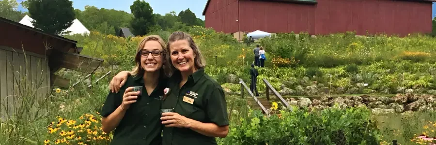 2 woemn holding drinks in front of a prairie garden