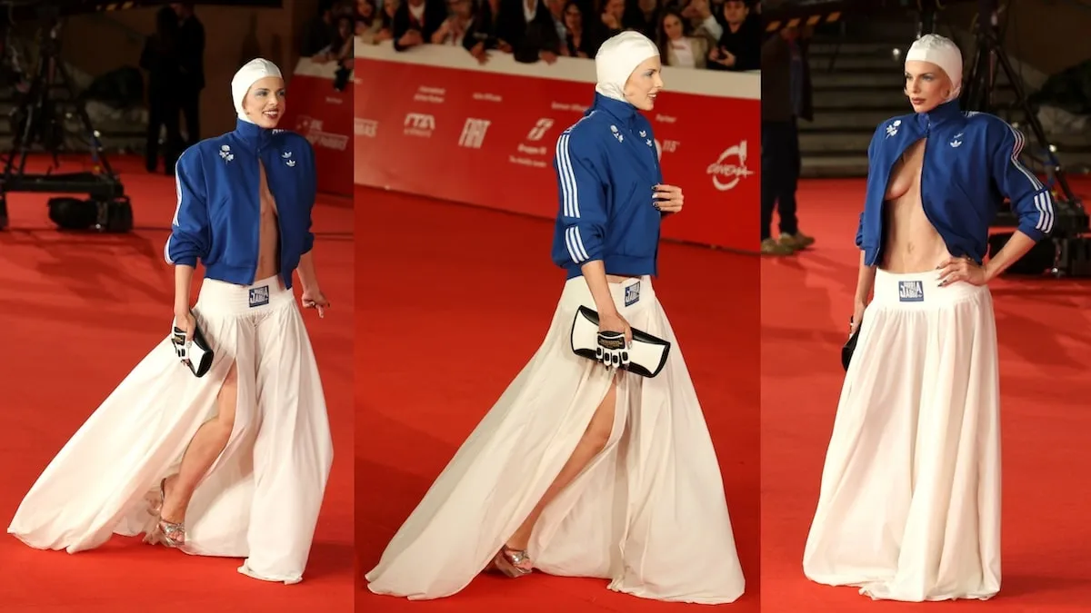 Wearing a white swim cap and blue Adidas jacket, Julia Fox poses for cameras on the red carpet at 'The Trainer' premiere