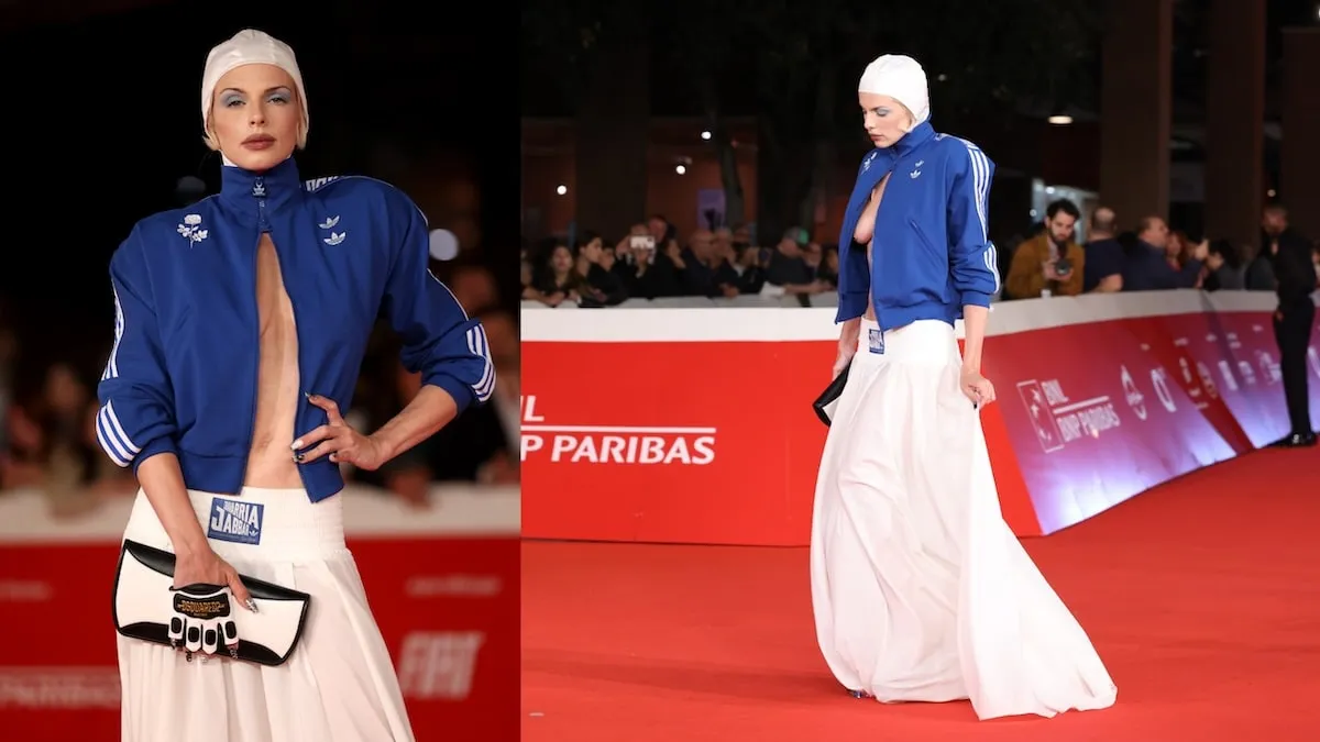 Wearing a white swim cap and blue Adidas jacket, Julia Fox poses for cameras on the red carpet at 'The Trainer' premiere