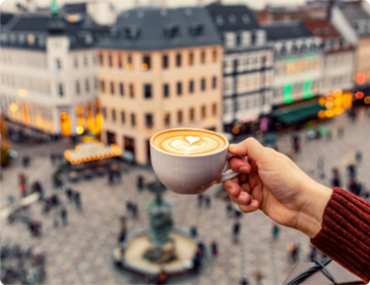 Coffee mug being held over an elevated view of a busy town.