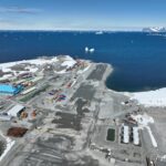 Aerial view of runway and large blue building and blue sea in background