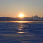 A sunset over a body of water with a mountain in the background