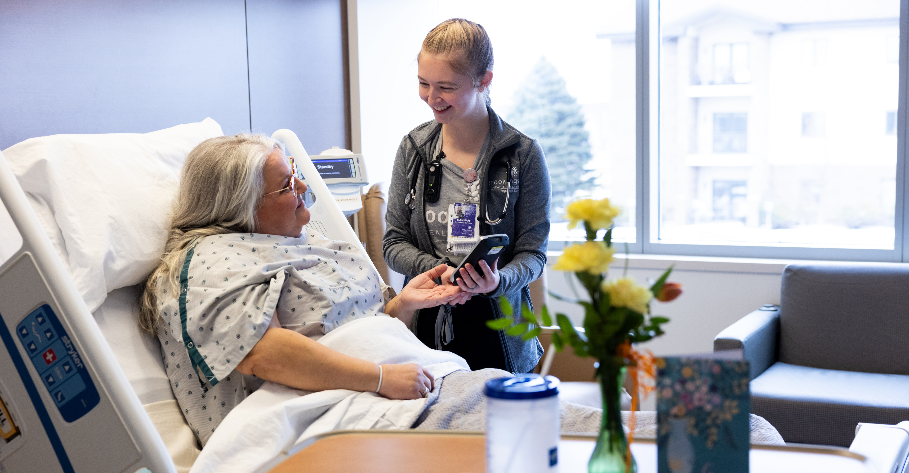 A female nurse cares for a female patient at bedside inside the an inpatient care room