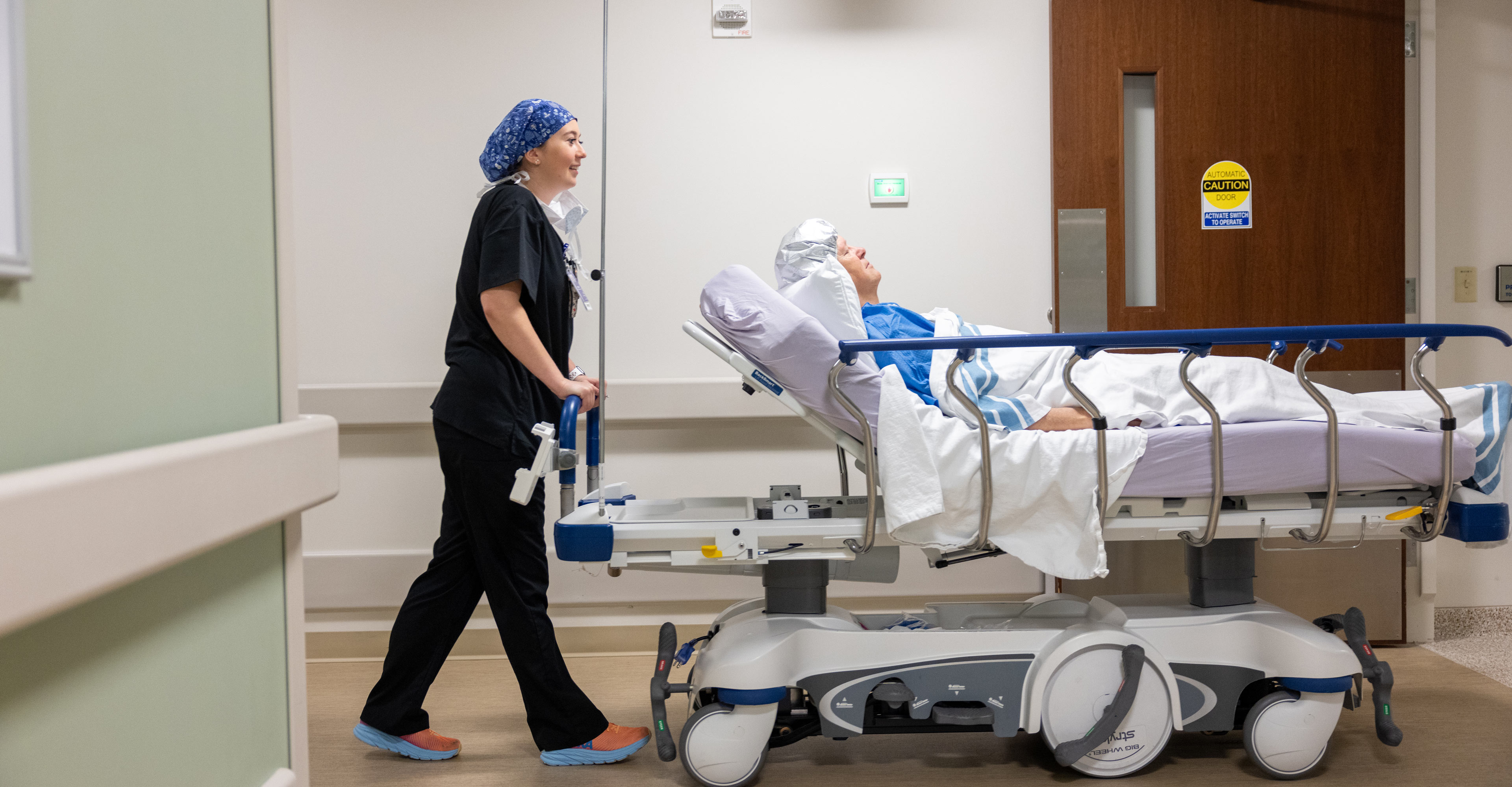 Female operating room nurse wheeling a male patient lying on a bed back to surgery