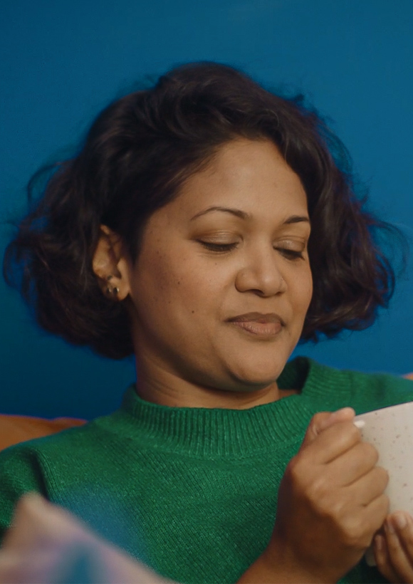 A young woman sat on a sofa looking at a cup of tea she is holding in her hands