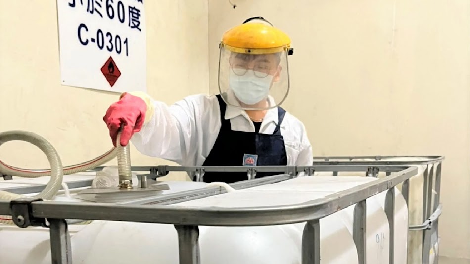 A supplier wearing red gloves, white shirt, black apron, mask, eyeglasses and face shield while handling a hose