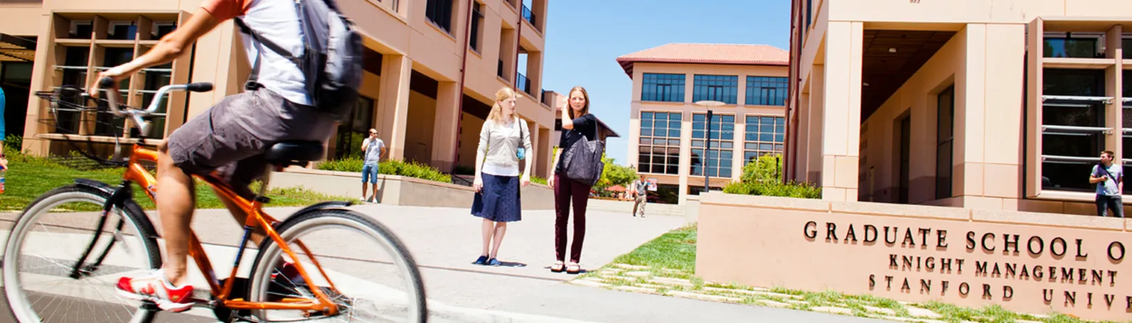 Students waiting to cross the street, bicyclist going by