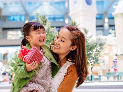 A mom carrying her daughter, who's holding a wrapped present