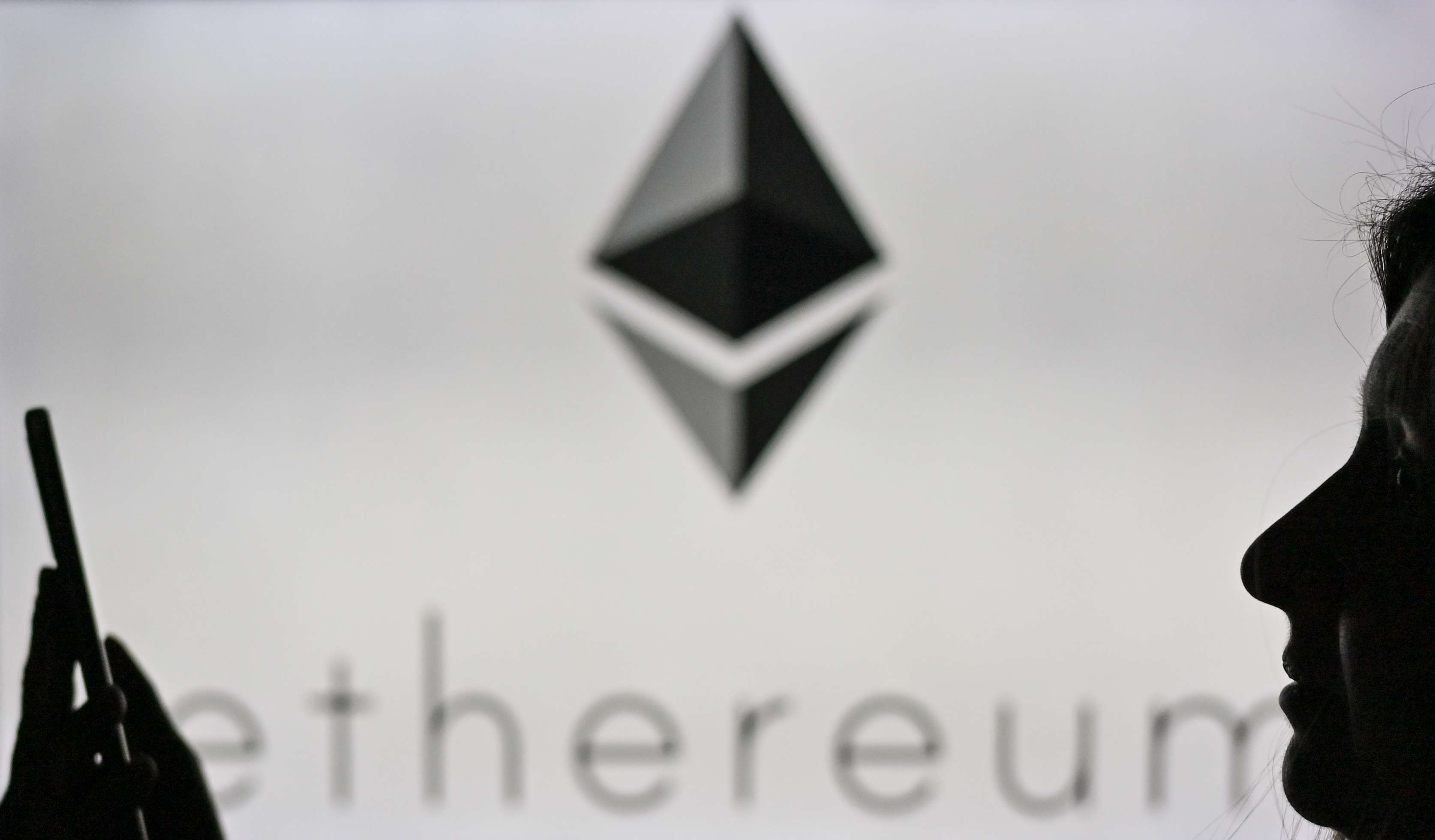 A woman holds a mobile device in front of the Ethereum logo. 