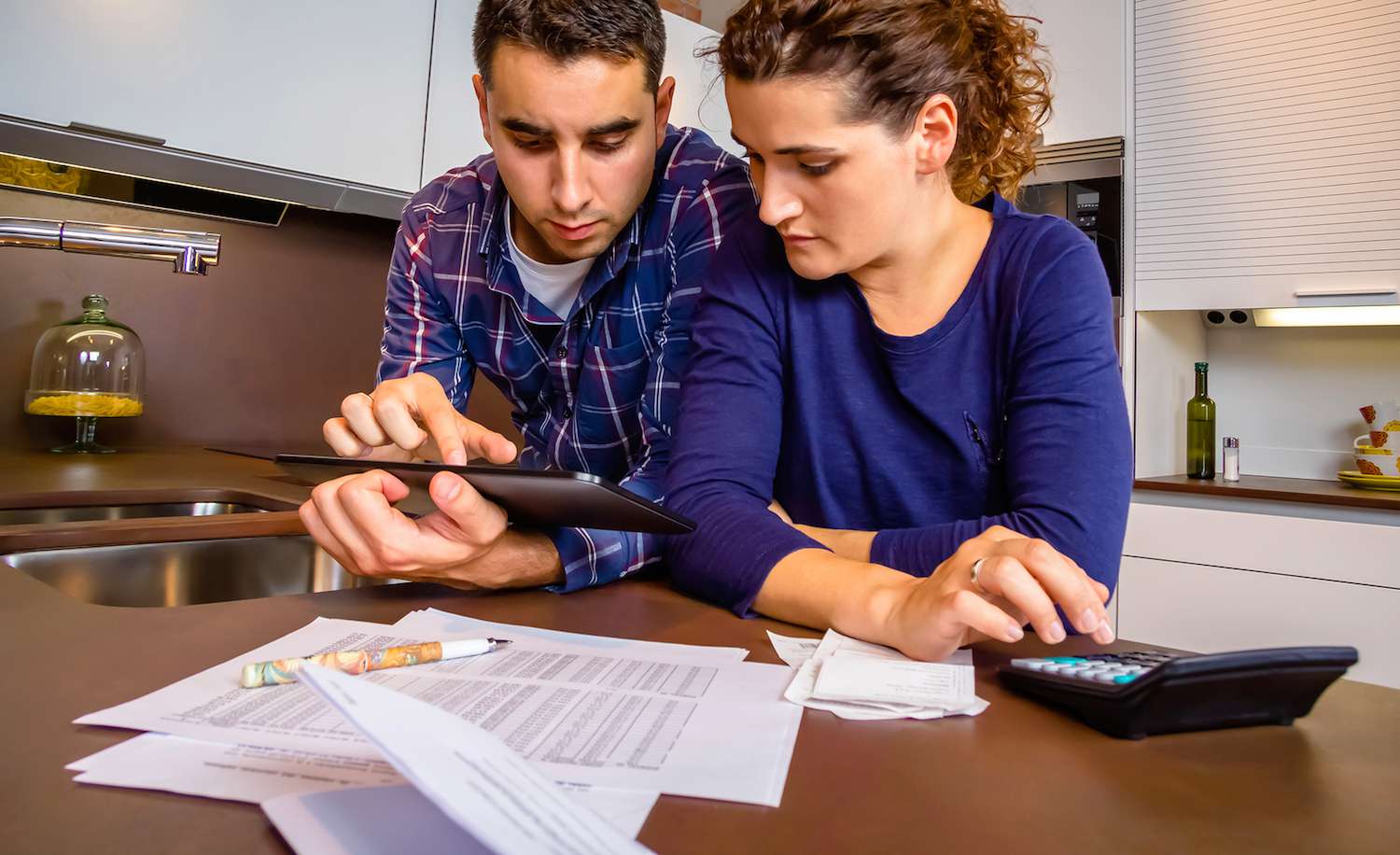 Worried young couple at kitchen table with papers and calculator