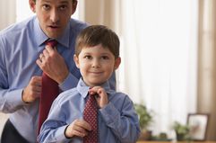 A man and a younger child putting on ties