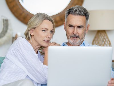 Older couple at home on living room couch, looking concerned at a laptop screen