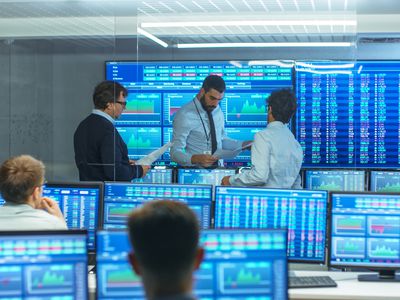 Three stock traders in front of computer screens talking with each other