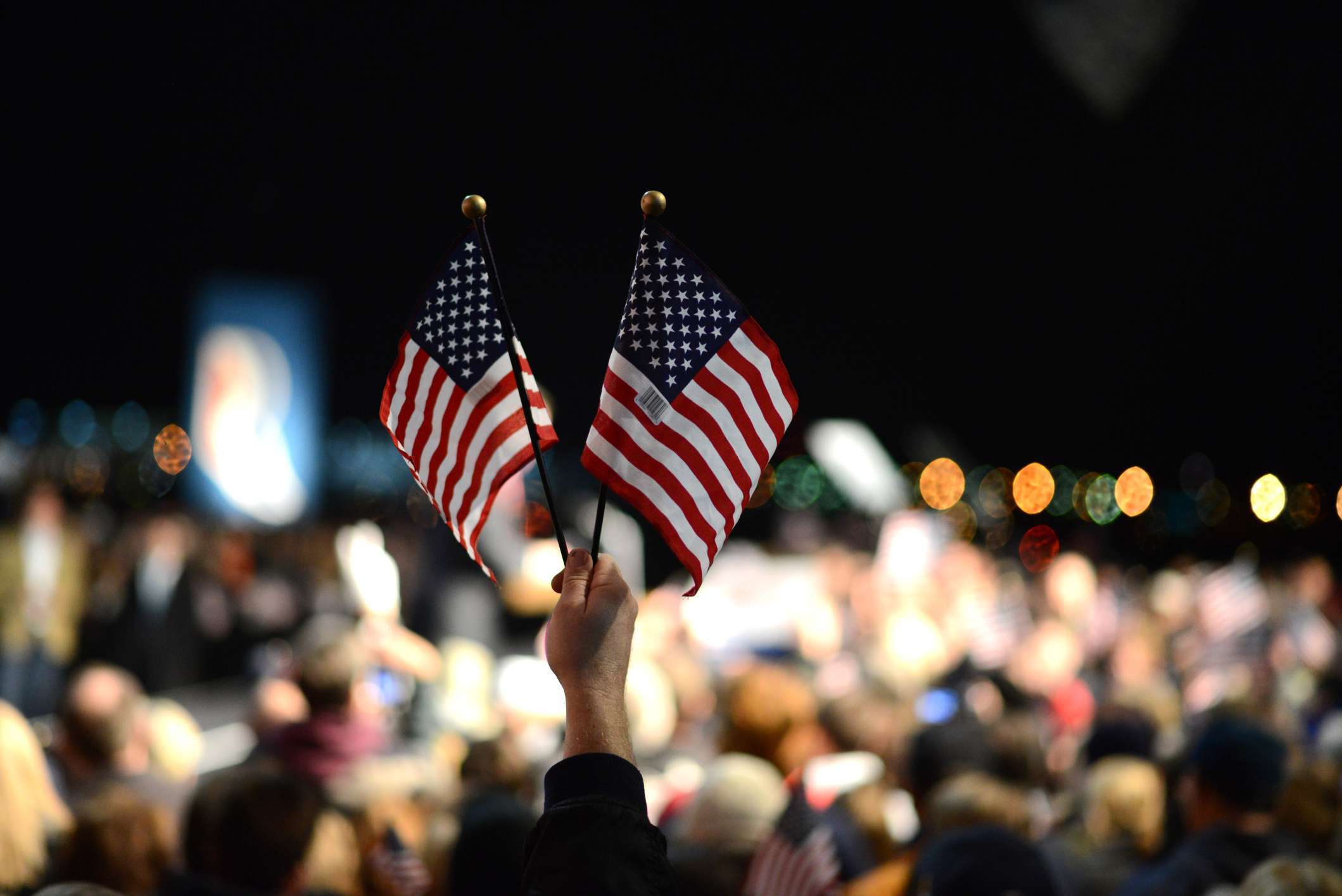 Two American flags held up by one hand in a sea of people. 