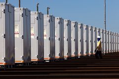 A technician wearing a helmet checks a long line of solar power equipment outdoors.