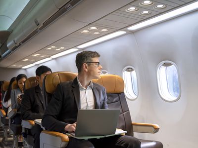 Person sitting in an airplane with a laptop and looking out the window