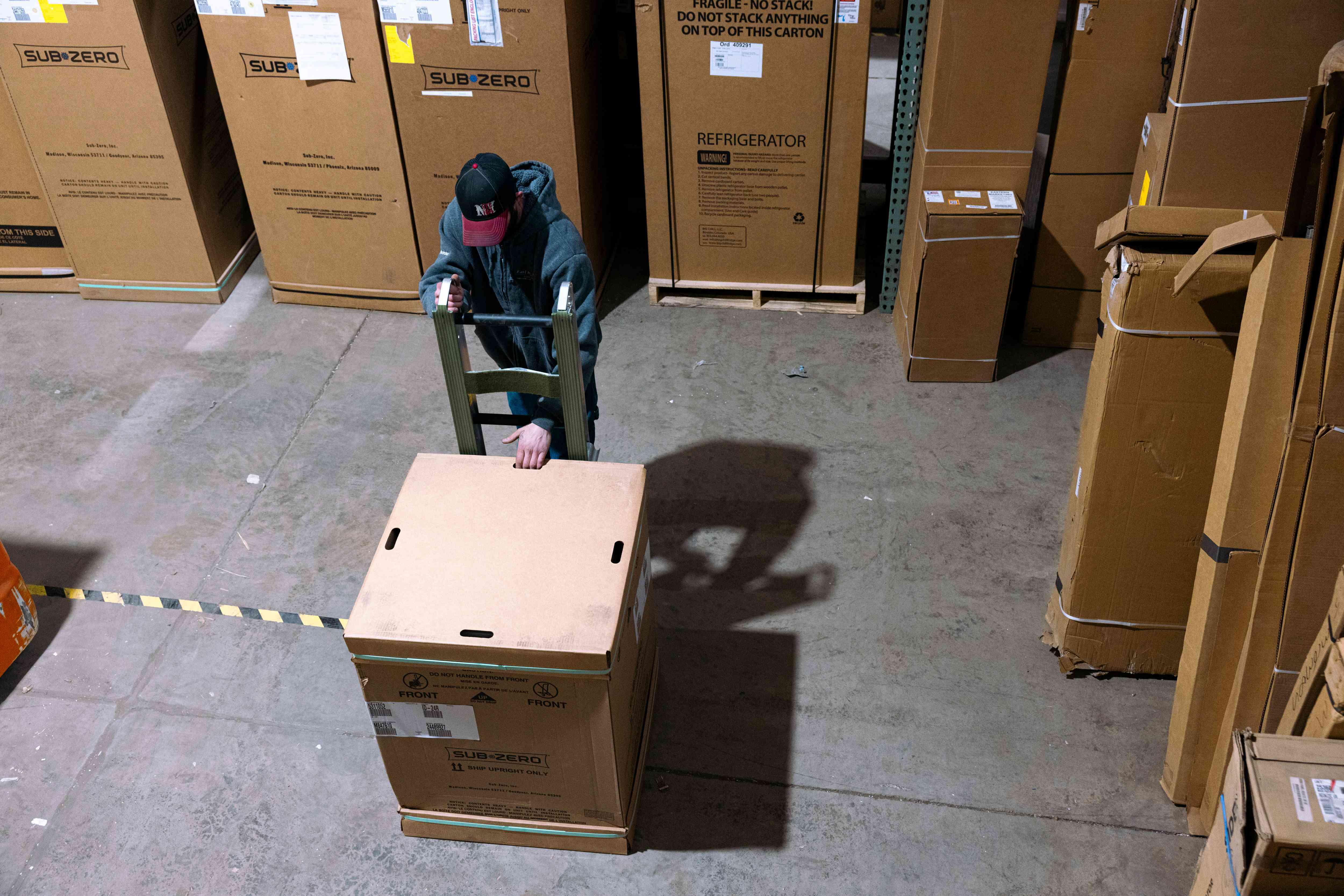 A worker in a warehouse moves a refrigerator in a box. 