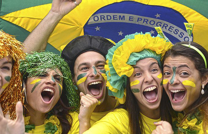 A group of young adults dressed up, probably for a soccer match, wearing the colors of Brazil and waving a Brazilian flag.