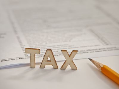 The word “TAX” in cut-out letters stands beside a pencil and federal income tax form.