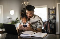 A man checks his investments on the computer with his child sitting in his lap