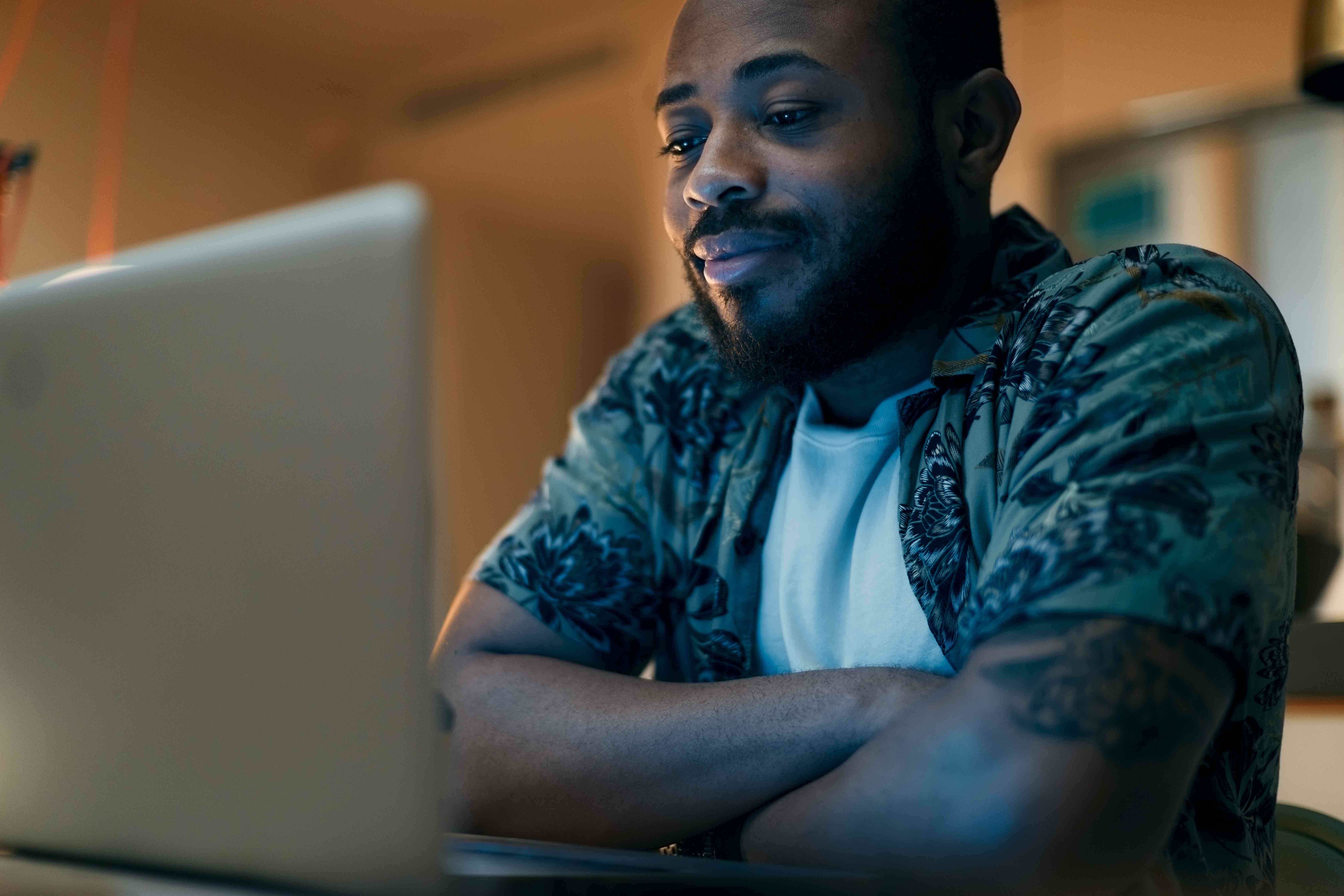 Man in his 20s or 30s sitting at home and looking at his laptop with a slight smile
