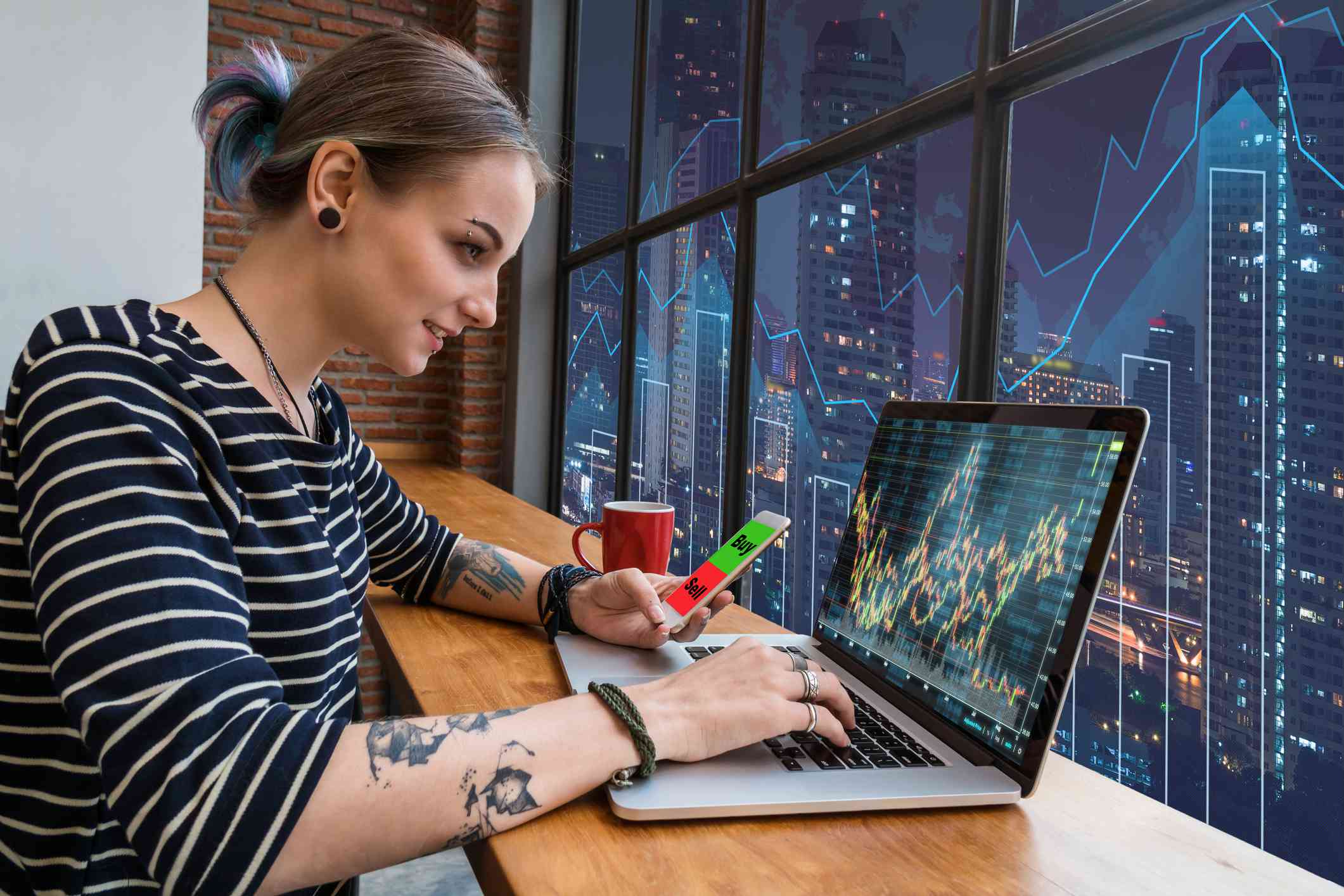 A young woman freelancer using the technology laptop and smart phone mobile showing trading graph with the stock exchange trading graph screen background.