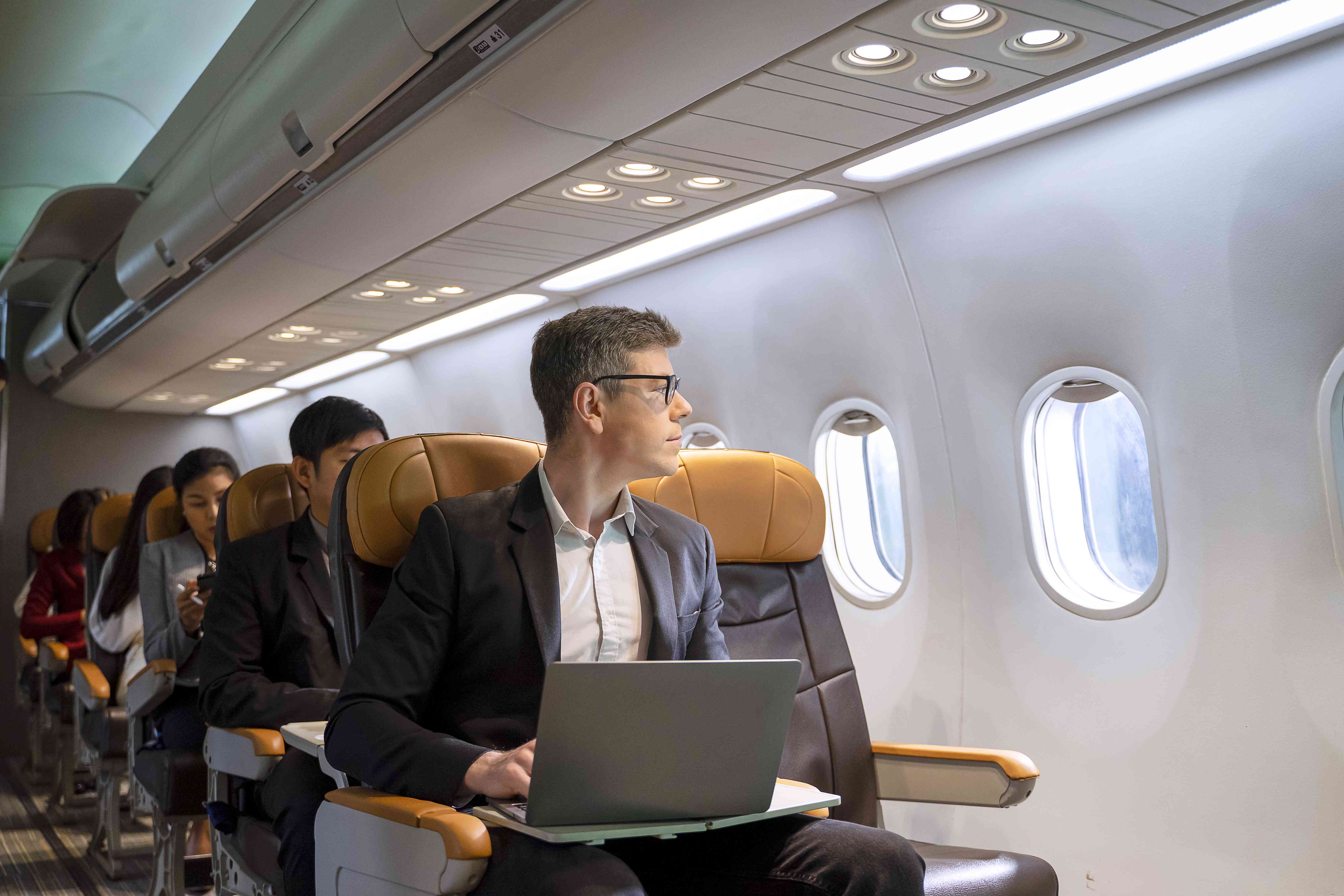 Person sitting in an airplane with a laptop and looking out the window