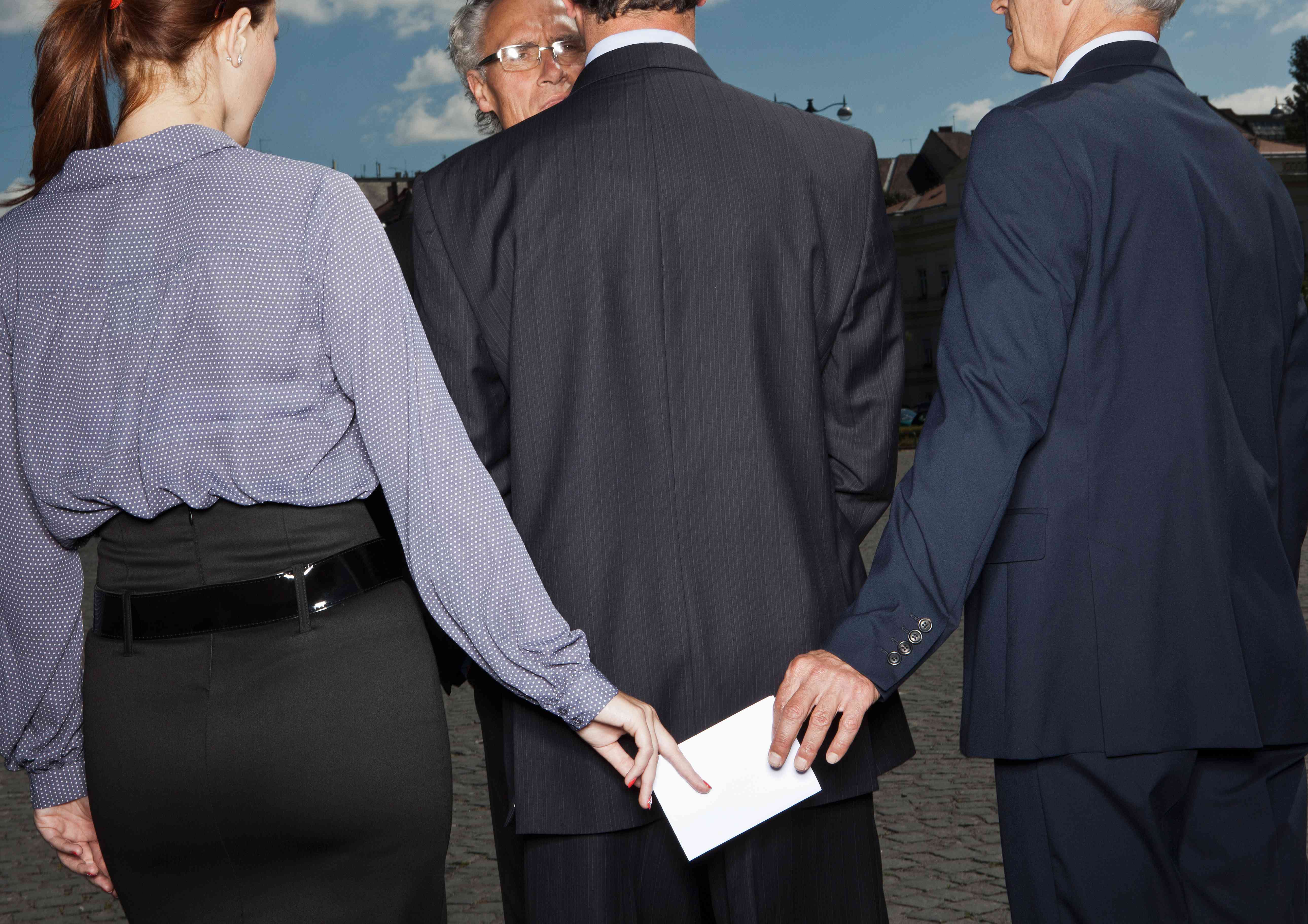 Man and woman passing an envelope behind the backs of 2 other people