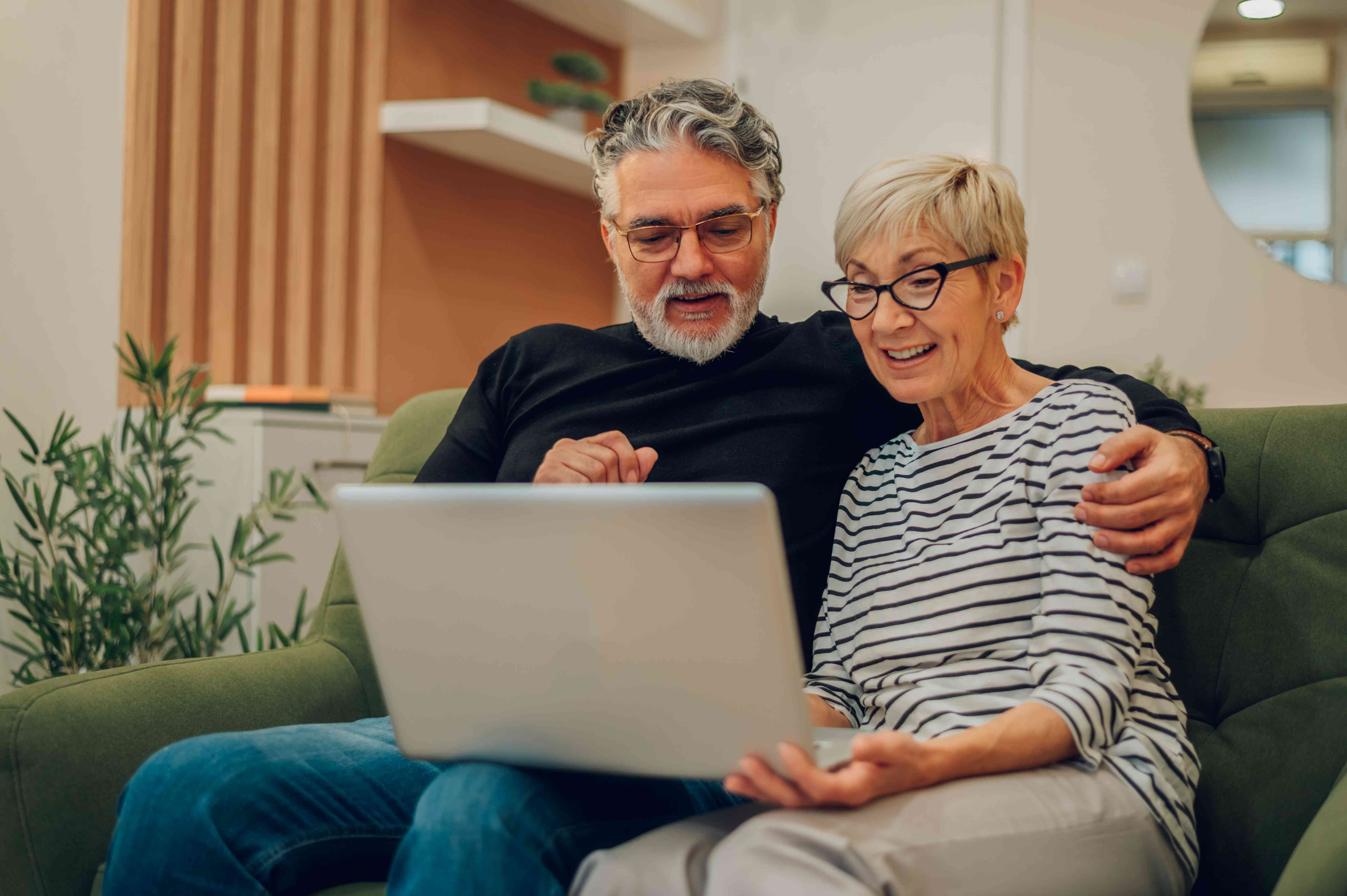 Older couple sitting on their couch and looking happily at something on their laptop screen